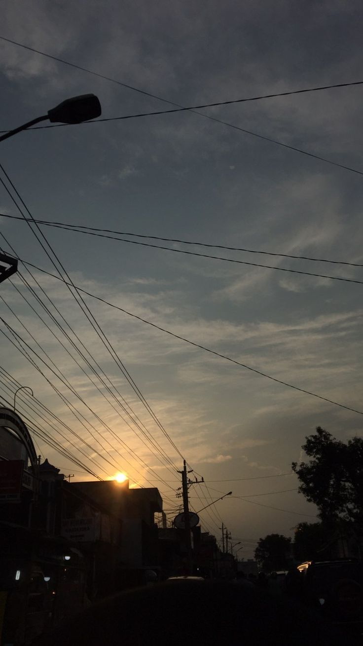 the sun is setting behind power lines and telephone poles in an urban area with cars parked on the street