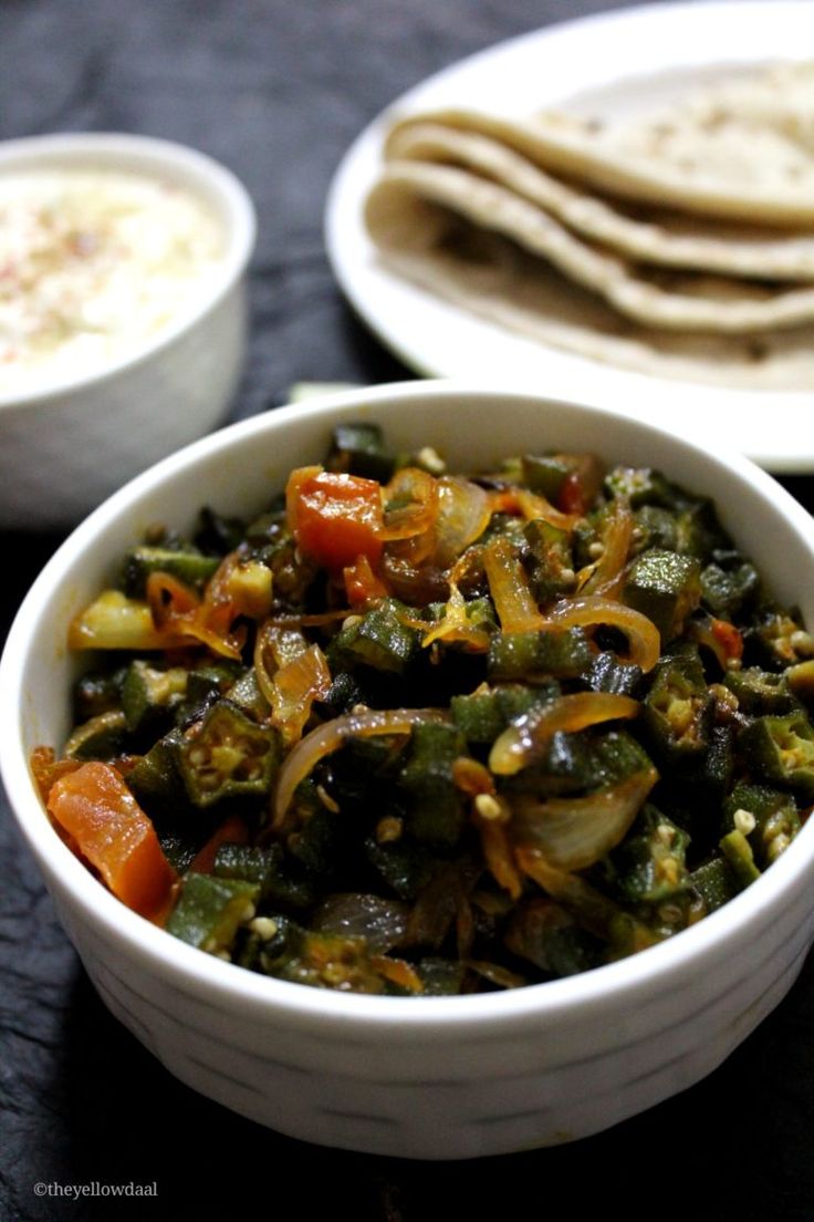 two bowls filled with different types of food next to pita bread and dipping sauce