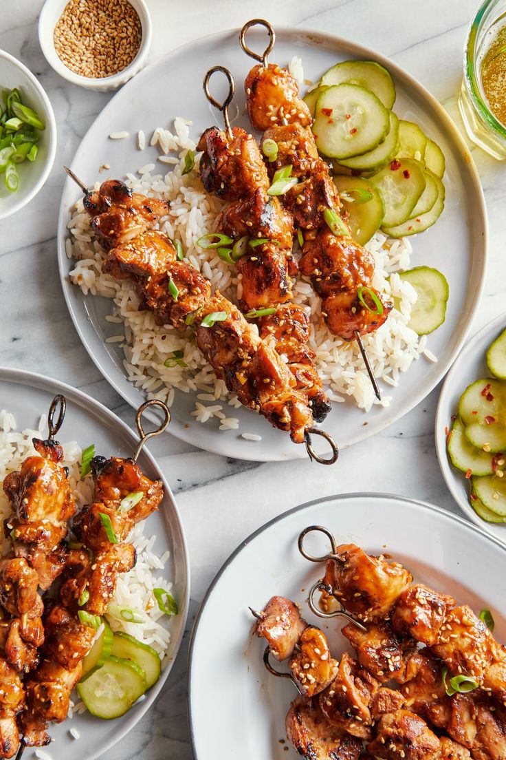 three plates with chicken skewers, rice and cucumber garnishes