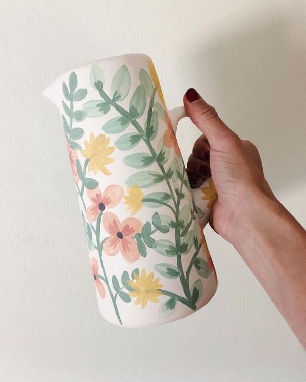 a hand holding a coffee mug with painted flowers on it and leaves around the cup