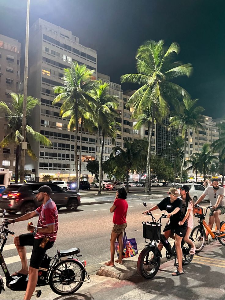 several people riding bikes on a city street at night with palm trees in the background