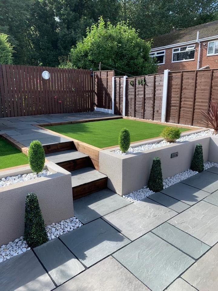 a modern garden with stone steps and grass in the center, surrounded by wooden fences