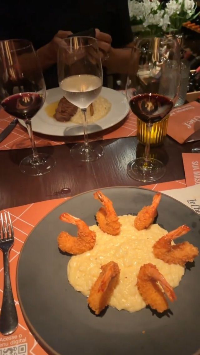 a plate with shrimp and grits on it next to wine glasses, utensils and plates