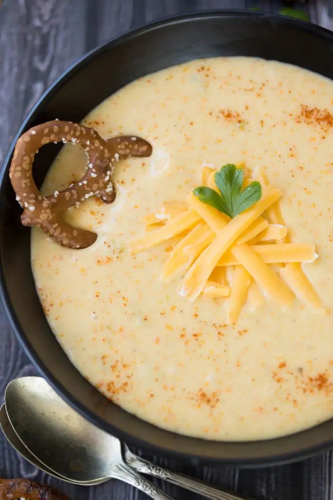 a bowl of cheese soup with pretzels on the side