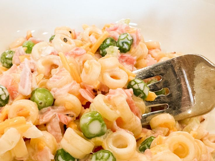 a close up of a fork in a bowl of pasta salad with peas and ham