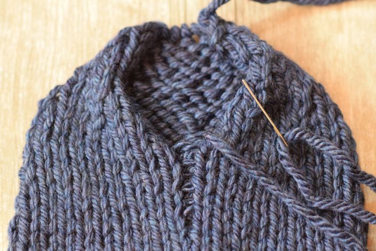 a close up of a knitted hat on a wooden surface with a pair of scissors