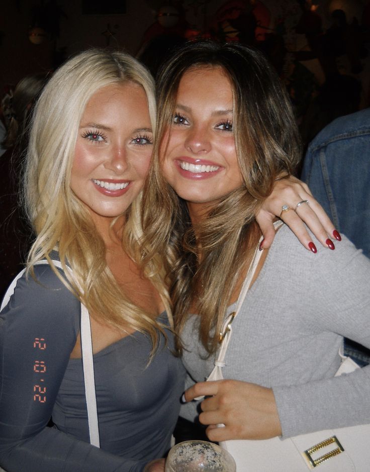 two beautiful young women standing next to each other at a bar smiling for the camera