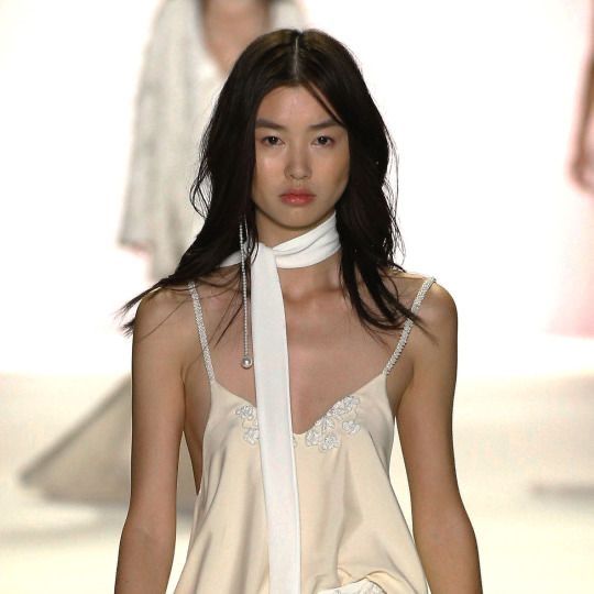 a model walks down the catwalk at a fashion show wearing a white dress and scarf