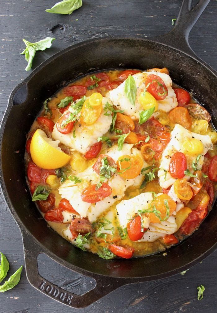 an iron skillet filled with fish and tomatoes