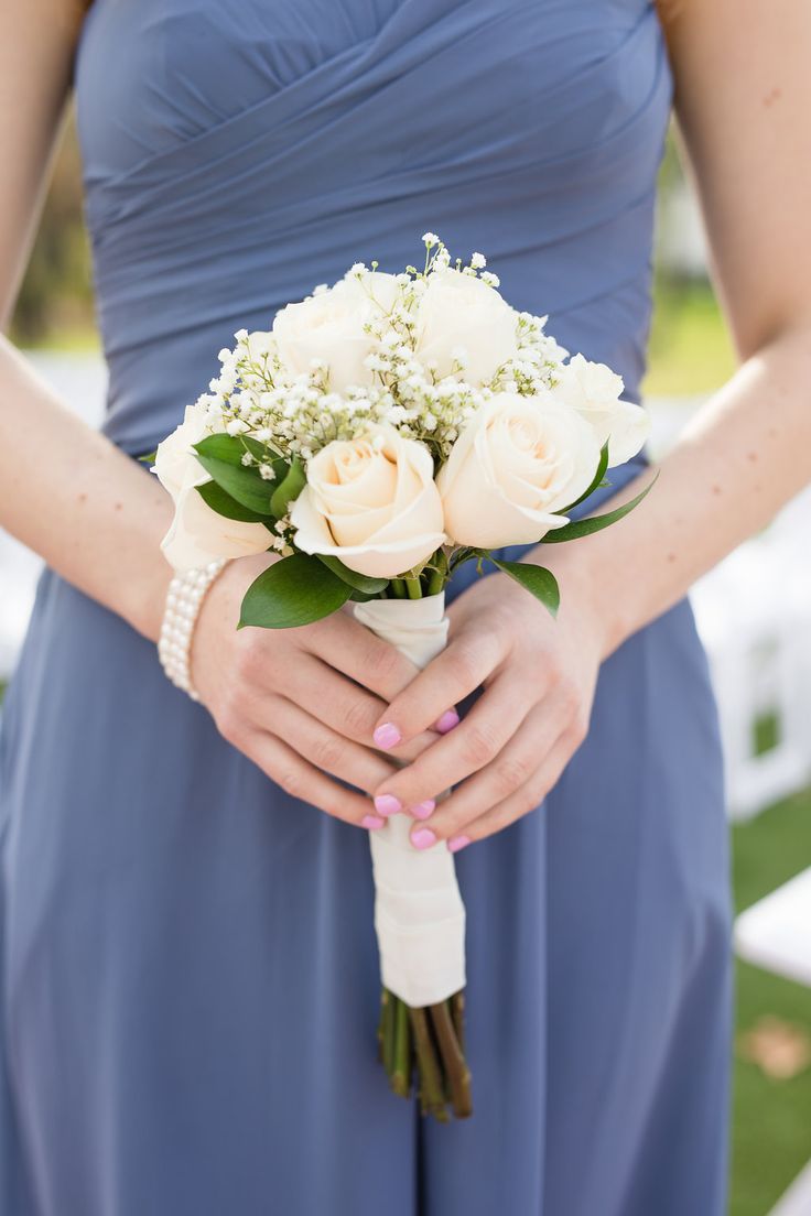 a woman in a blue dress holding a bouquet of white roses and baby's breath