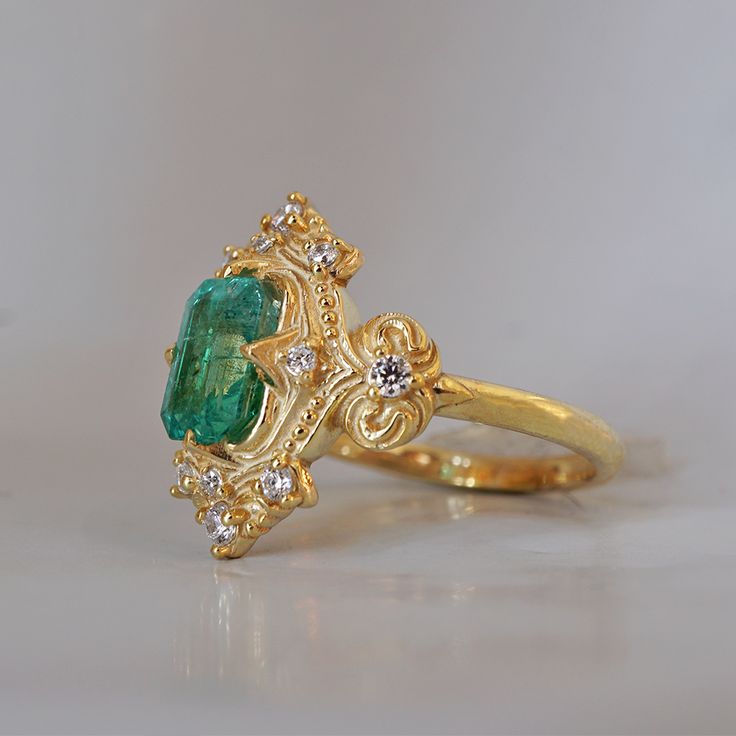 a gold ring with an emerald and diamond accenting the center, sitting on a white surface