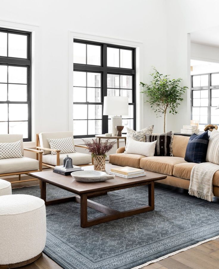 a living room with couches, chairs and tables in front of two large windows