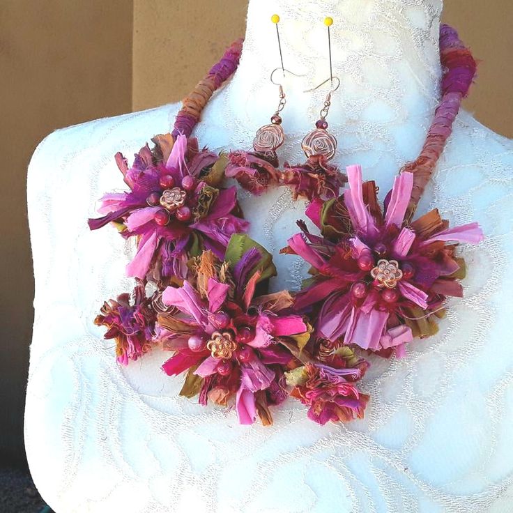 a white mannequin with pink flowers on it's neck and two pairs of earrings