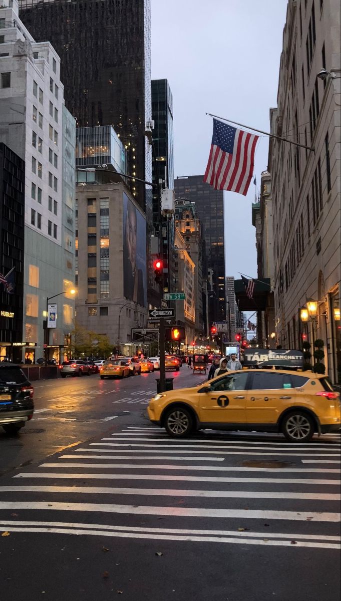 a yellow taxi cab driving down a street next to tall buildings with american flags on them