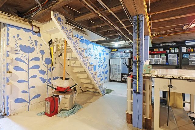 an unfinished room with blue and white flowers on the wall, stairs leading up to it