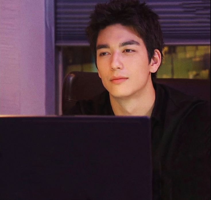 a young man sitting in front of a laptop computer looking at the screen while wearing a black shirt