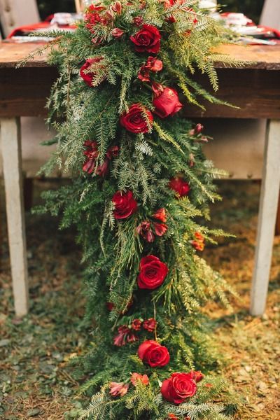 a table with red flowers and greenery on it, next to a wooden bench