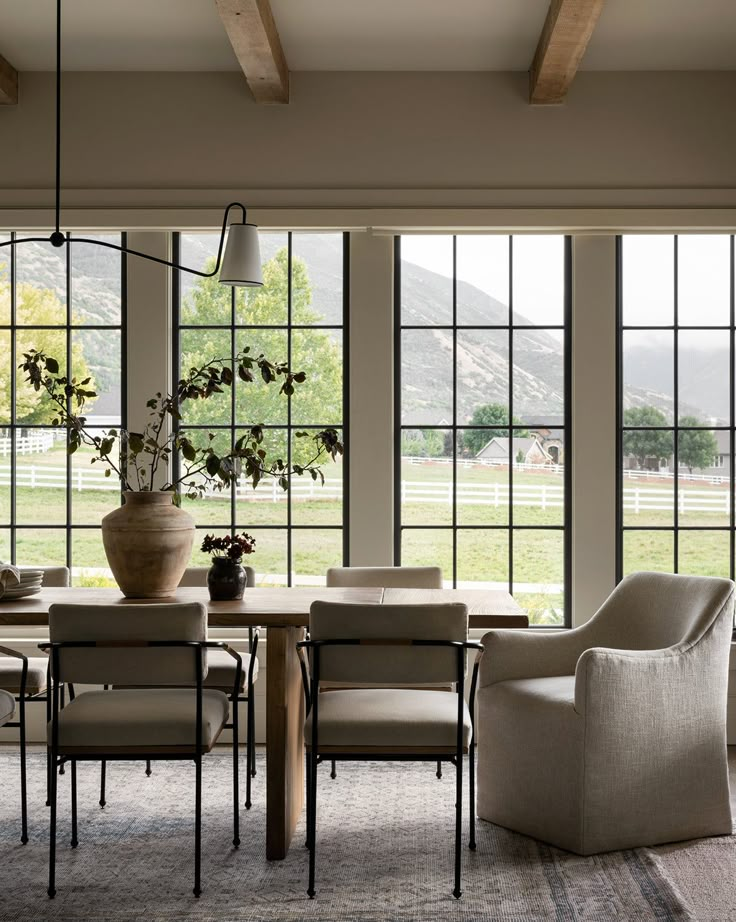 the dining room table is surrounded by chairs and vases with flowers in them, along with large windows that look out onto a grassy field