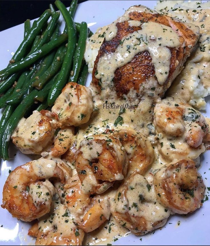 a white plate topped with chicken and shrimp covered in gravy next to green beans