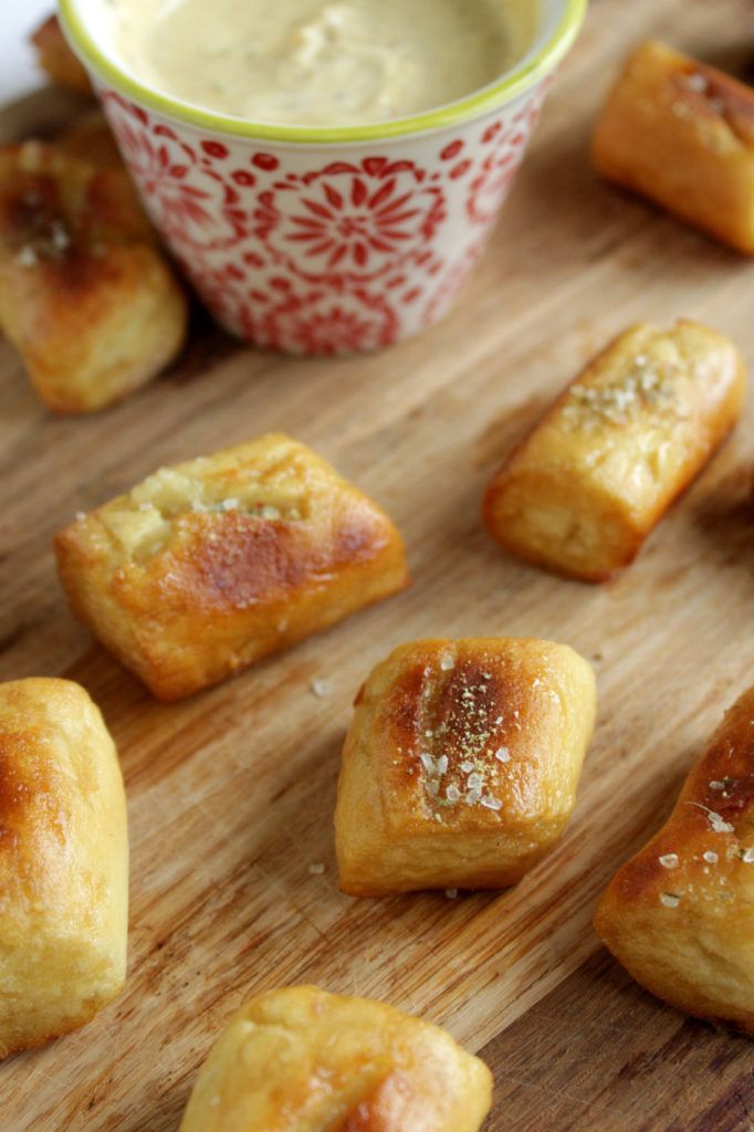 small pastries on a wooden cutting board next to a bowl with dip in it