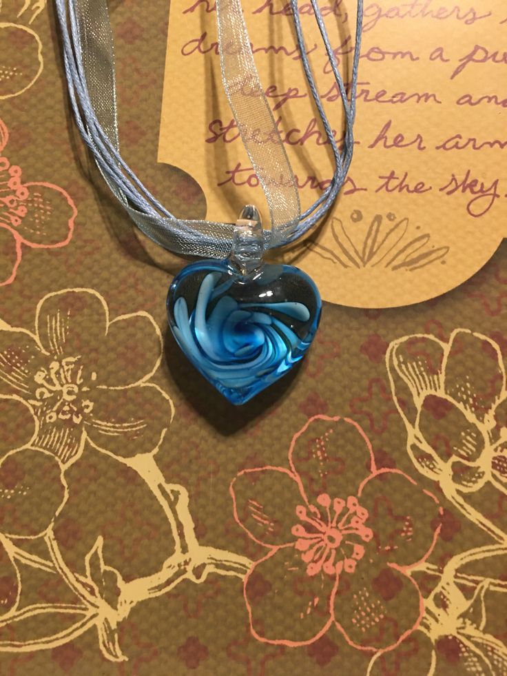 "Glass heart with a swirl of ocean blue. Heart is 1\" across x 1\". Necklace is 8\" closed." Heart-shaped Light Blue Jewelry For Valentine's Day, Blue Heart Charm Necklace For Gift, Blue Heart Charm Necklace For Valentine's Day, Blue Heart Necklace For Anniversary, Blue Heart Necklace With Charm For Anniversary, Blue Open Heart Necklace For Gift, Adjustable Blue Necklace For Anniversary, Blue Open Heart Jewelry Gift, Blue Adjustable Necklace For Valentine's Day