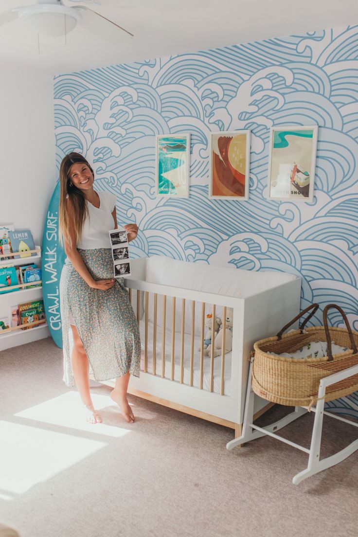 a woman standing next to a baby crib in a room with blue waves on the wall