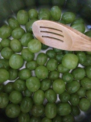 peas are being cooked in a pot with a wooden spoon