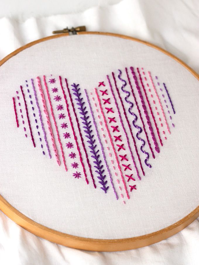 a cross stitch heart is shown on a white surface with a wooden hoop holding it