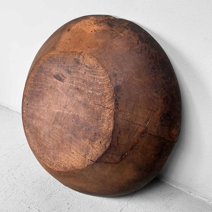 a large wooden bowl hanging on the wall next to a white wall with a cement floor