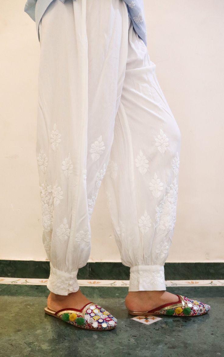 Introducing our Rayon White Afghani Chikankari Embroidered Pants, the epitome of elegance and comfort. Crafted with meticulous attention to detail, these pants showcase the timeless art of Chikankari embroidery, a delicate and intricate technique originating from the Indian subcontinent. The Afghani-style silhouette adds a touch of uniqueness, with its wide legs and relaxed fit, providing freedom of movement and a flattering drape. The Chikankari embroidery adorns the pants with exquisite floral patterns, meticulously handcrafted by skilled artisans. This intricate embroidery elevates the overall design, adding a touch of sophistication and cultural richness. Whether paired with a simple top for a relaxed bohemian look or dressed up with a stylish blouse for a more refined ensemble, our Ra Afghani Pants Woman, Traditional Embroidered Ankle-length Bottoms, Elegant Chikankari Embroidery Sets With Straight Pants, Elegant Festive Pants With Floral Embroidery, Elegant Floral Embroidered Festive Pants, Elegant Floral Embroidered Pants For Festive Occasions, Elegant Pants With Intricate Embroidery For Festive Occasions, Elegant Wedding Pants With Intricate Embroidery, Traditional White Bottoms