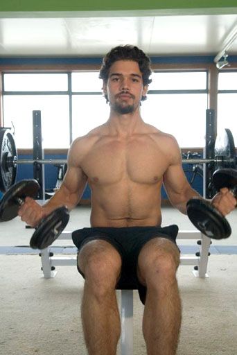 a shirtless man is sitting on a bench with two dumbbells