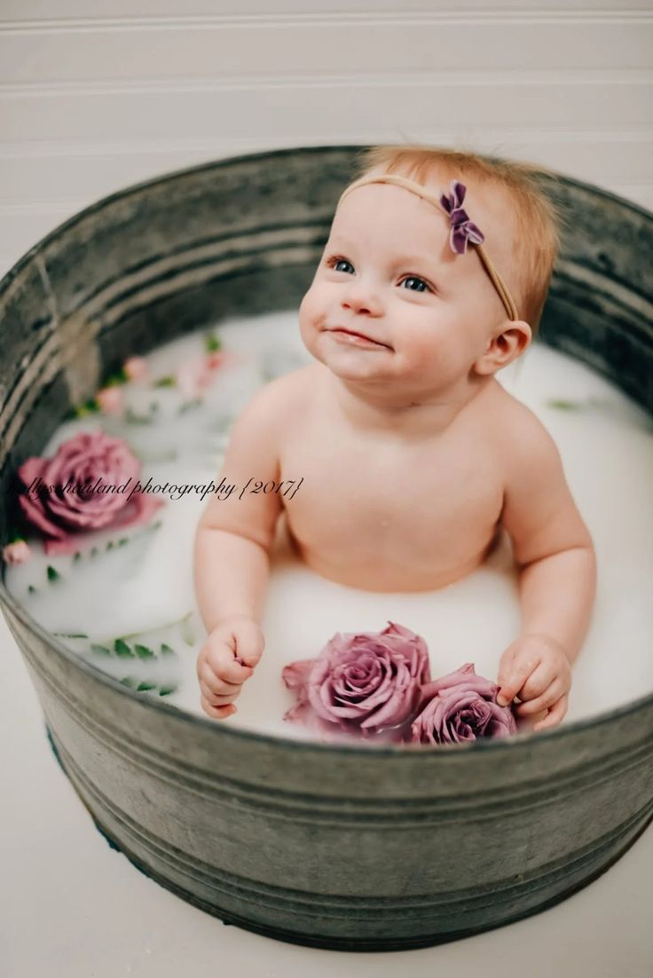 a baby sitting in a tub filled with water and pink roses on it's head