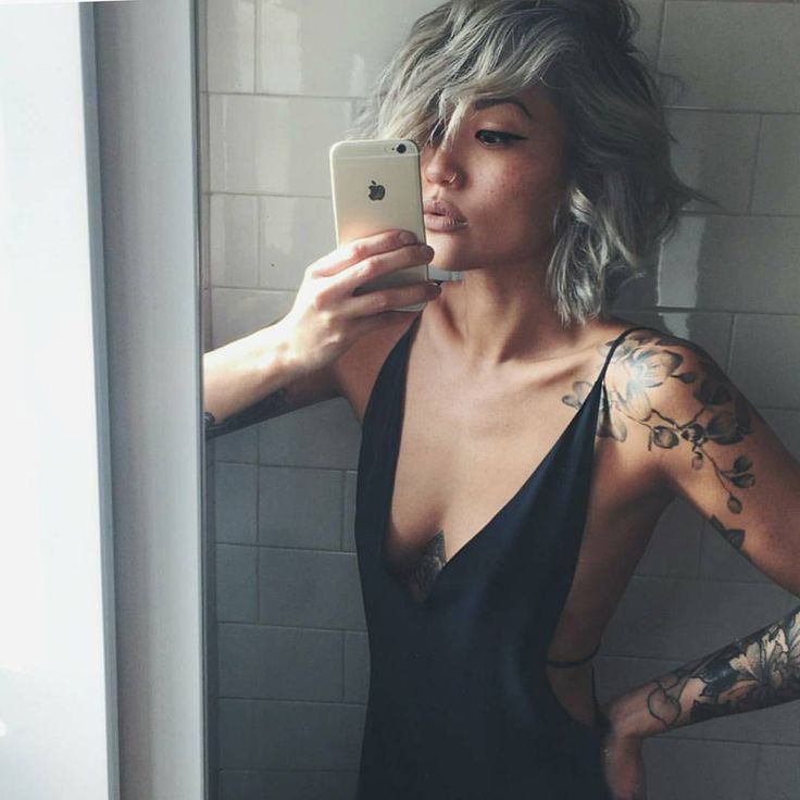 a woman with tattoos taking a selfie in the mirror while wearing a black dress