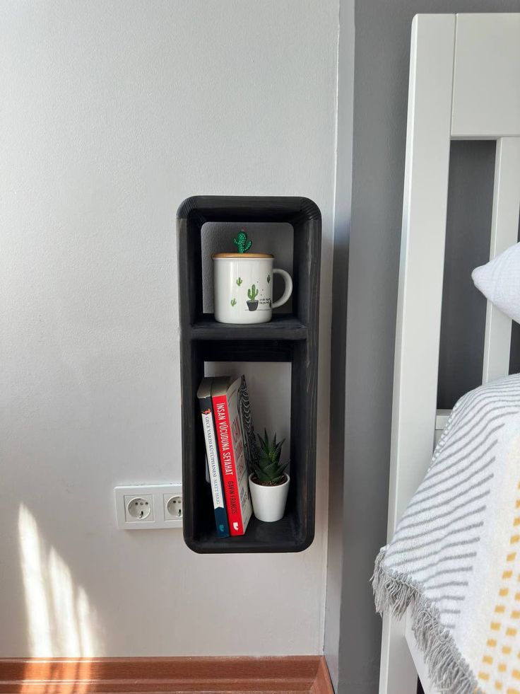 a shelf with books and coffee cups on it next to a white bed in a bedroom