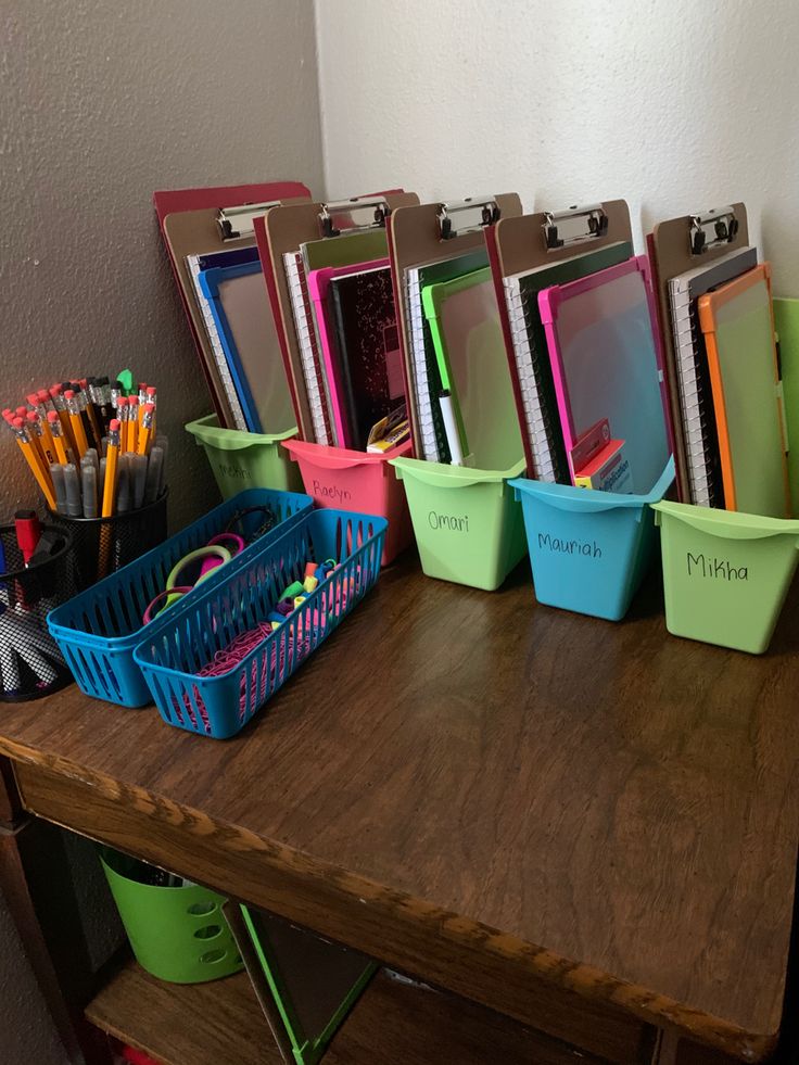 there are many different colored bins on the table with pens and pencils in them