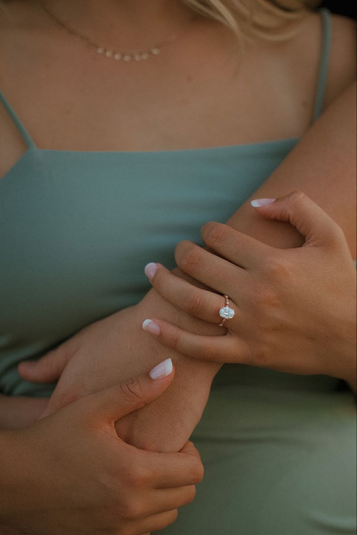 a woman in a green dress holding her hand on her chest and wearing a ring