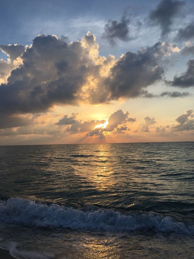 the sun is setting over the ocean with clouds