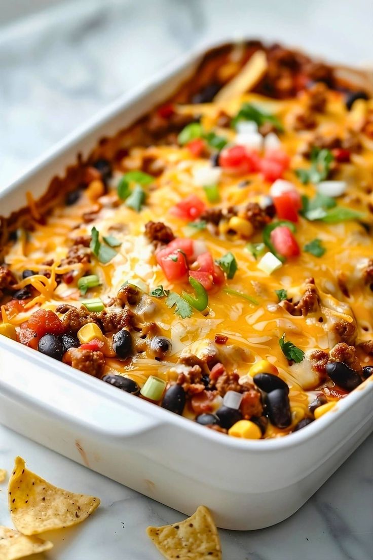 a white casserole dish filled with taco meat, cheese and black beans