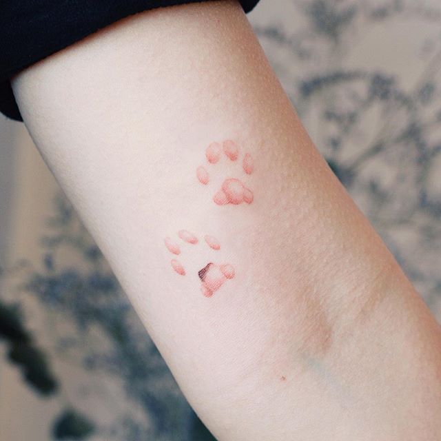 a person with a small tattoo on their arm that has pink paw prints all over it