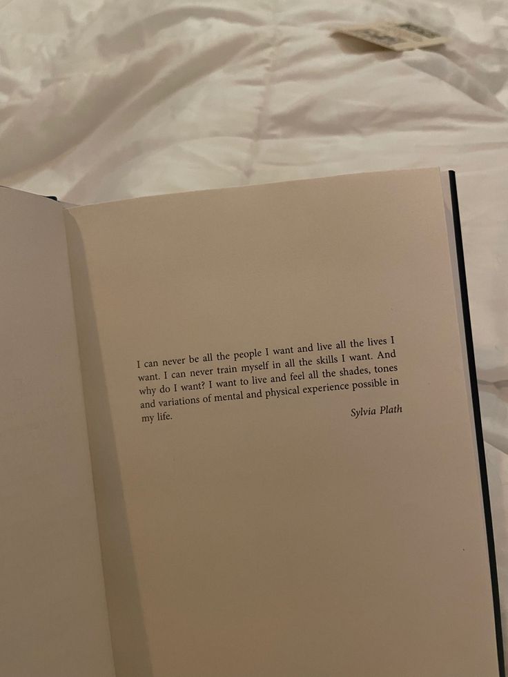 an open book sitting on top of a bed next to a white sheet covered wall