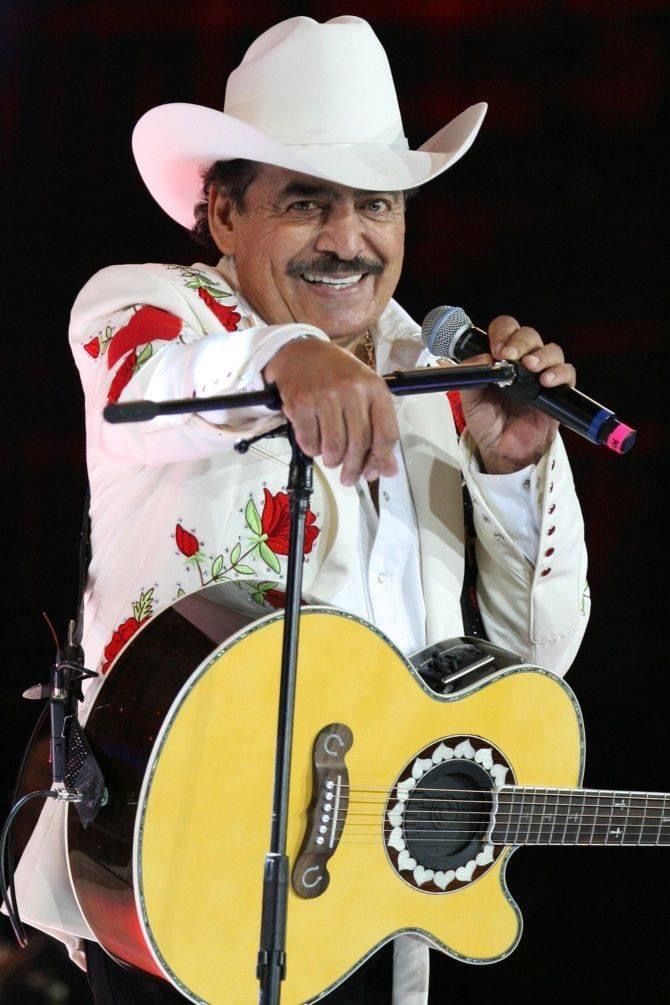 a man wearing a cowboy hat holding a guitar and singing into a microphone on stage