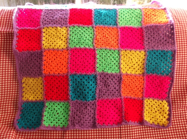 a colorful crocheted blanket sitting on top of a red and white checkered table cloth