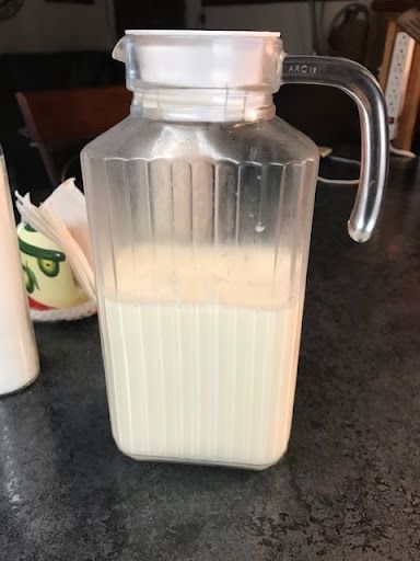 a pitcher filled with milk sitting on top of a counter next to a bottle of milk