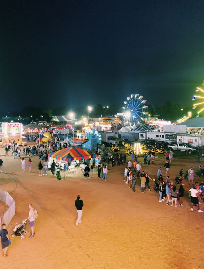 an aerial view of a fair at night with people walking around and carnival rides in the background