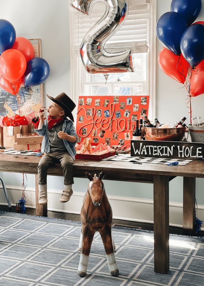 a boy is sitting on a table with balloons in the shape of two and a horse