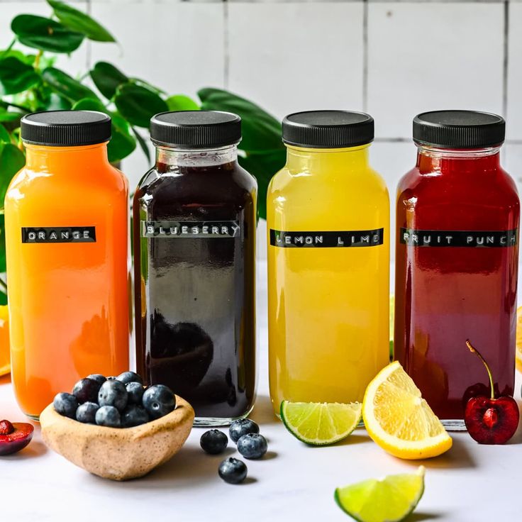 several different types of juices are lined up on a table with lemons, blueberries, and cherries