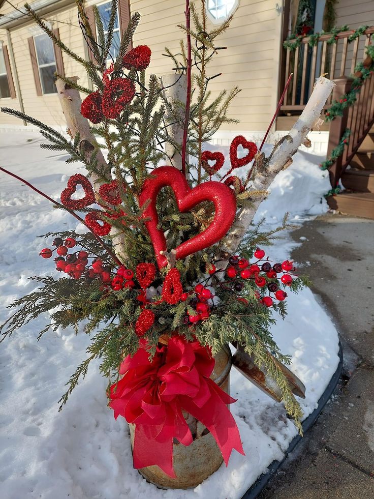 a vase filled with red flowers and greenery sitting on top of snow covered ground