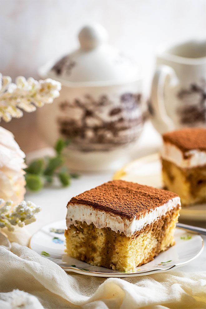 a piece of cake on a plate next to a cup and saucer with flowers in the background