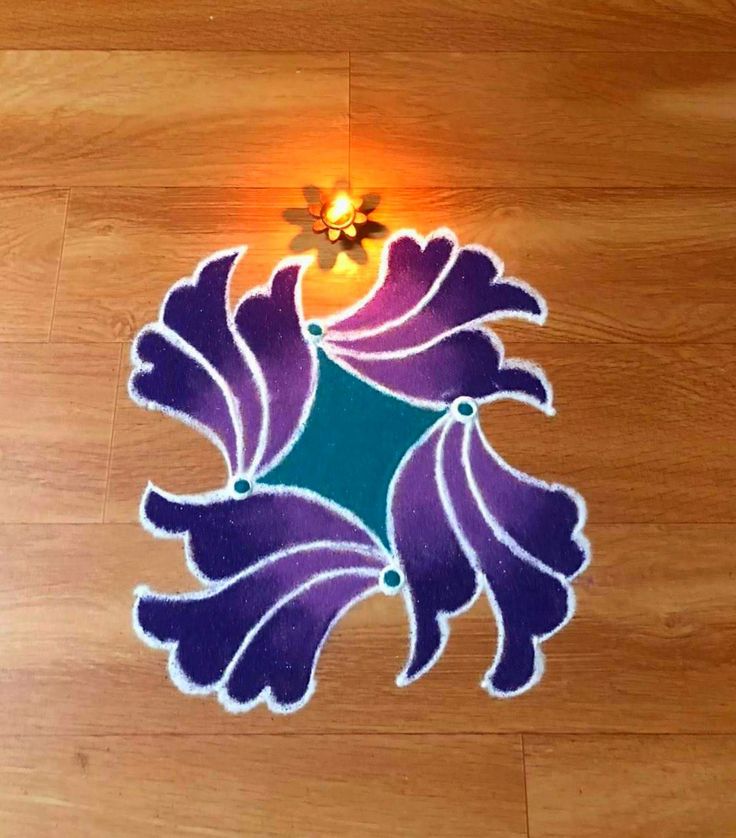 a small purple and green flower sitting on top of a wooden floor next to a light