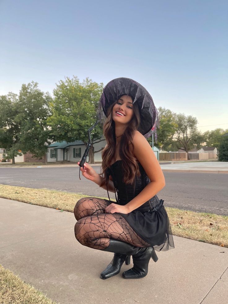 a woman kneeling down on the sidewalk with an umbrella over her head and holding something in her hand